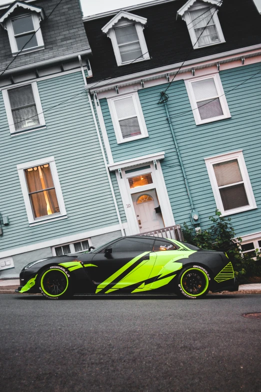 a sports car with bright neon green wheels is parked near some blue and gray buildings