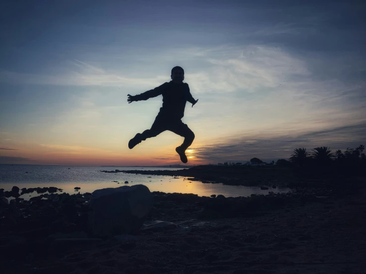 silhouette of person jumping up on beach with sun setting in background