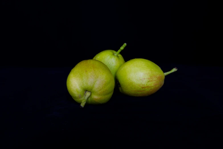 three green apples on black background and one yellow fruit in front