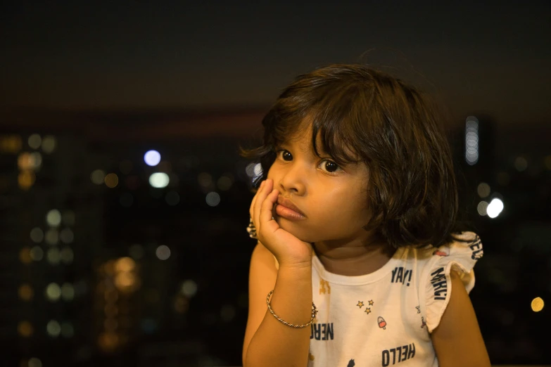 small child with hand on chin standing in front of a cityscape