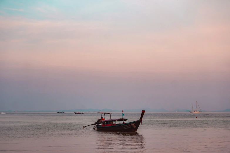 a small boat sitting in the ocean under a pink sky