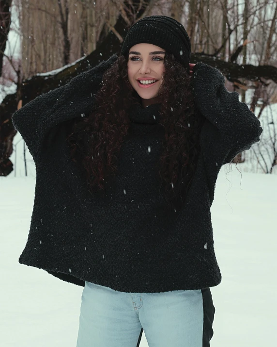 a young woman standing in the snow next to trees