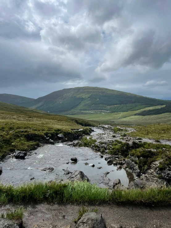 an overcast sky over a mountain and stream in the distance