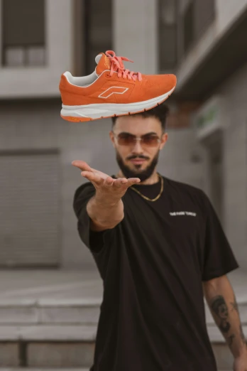 a man in a black shirt is balancing an orange sneaker on his head