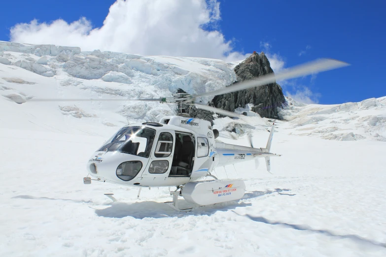 a white helicopter on the snow with a mountain in the background