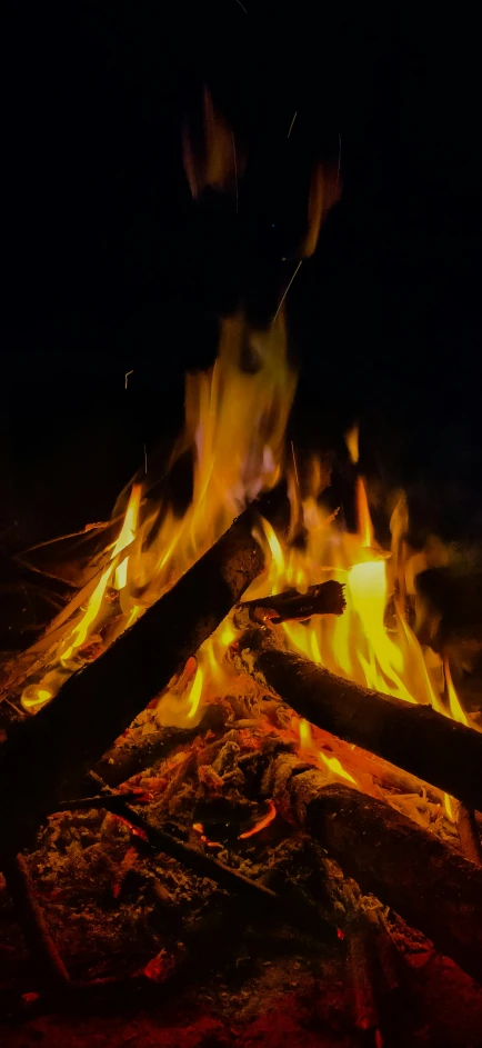 a bonfire burning in the dark surrounded by wood