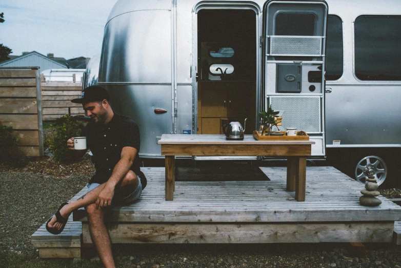 a man sitting at a table by a small travel trailer