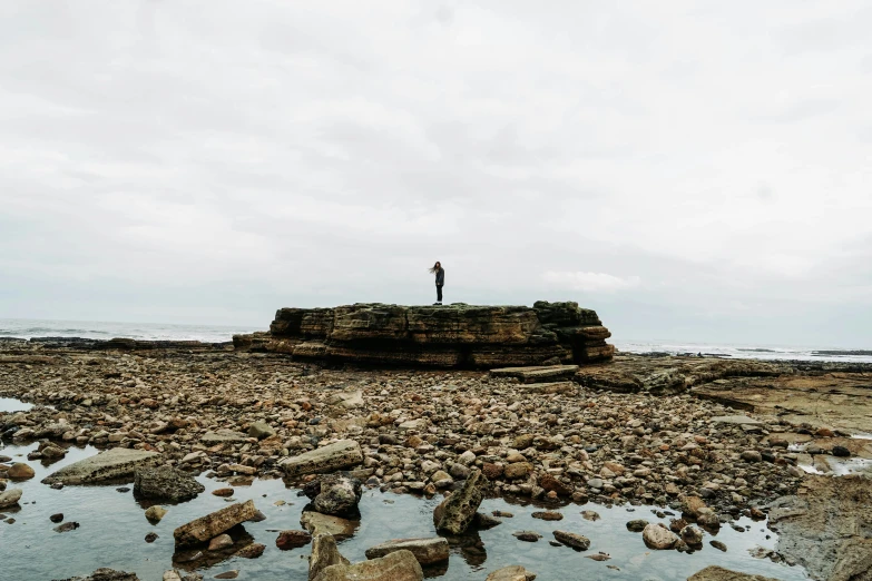 a man standing on a rocky shoreline next to water