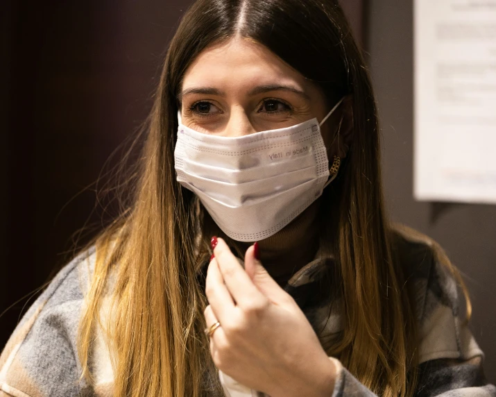 a woman in a mask and grey sweater puts on a face mask
