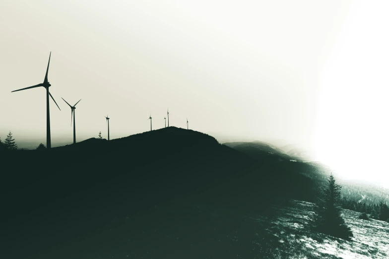 wind turbines are standing near the mountains on a misty day