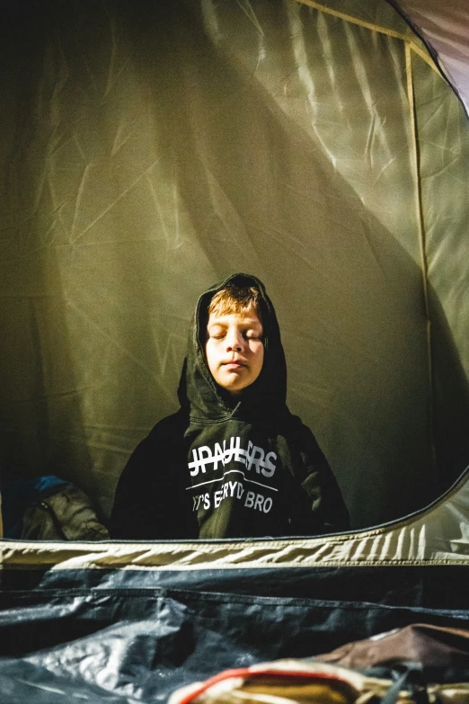 the boy is inside of the tent on the floor