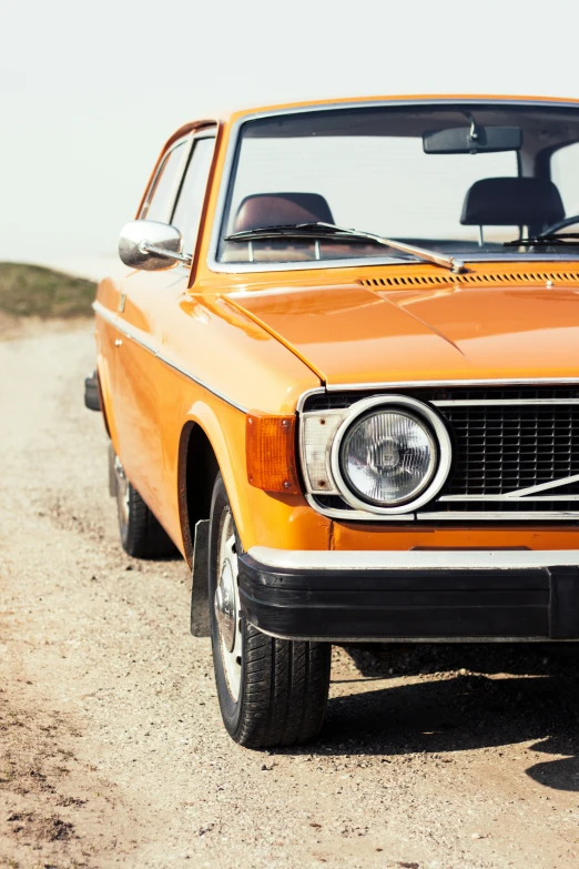 an orange car sitting on the side of a dirt road