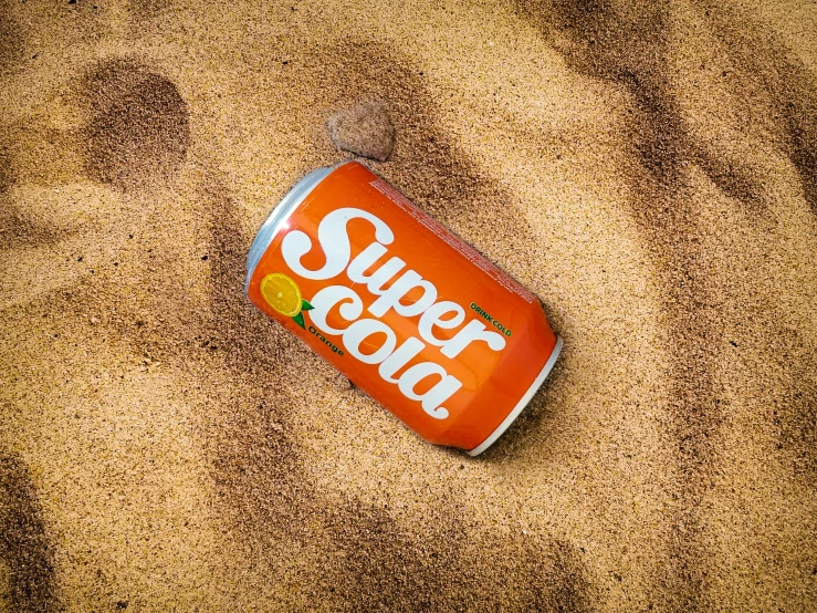 a can on the sand with the word super cola on it