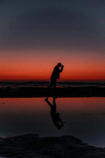 a man in silhouette walking next to the ocean during a red sunset