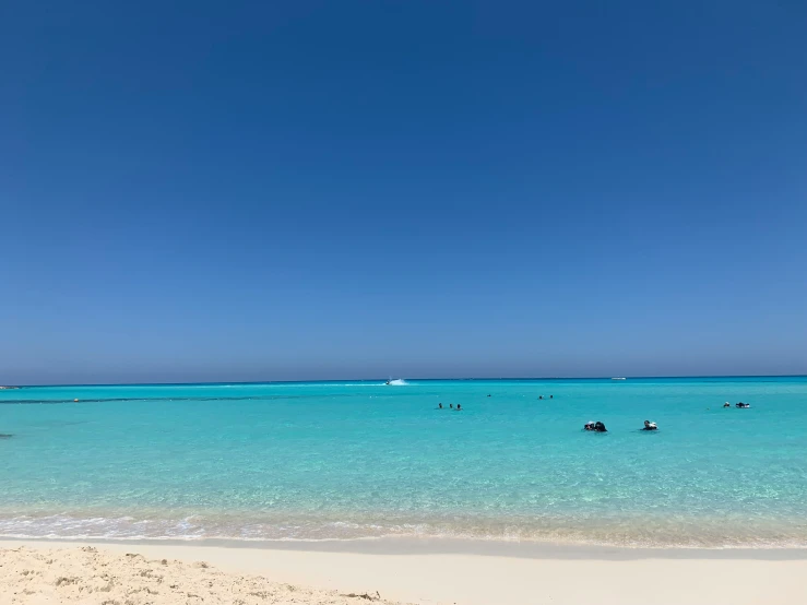 people playing in the ocean and some boats out on the water