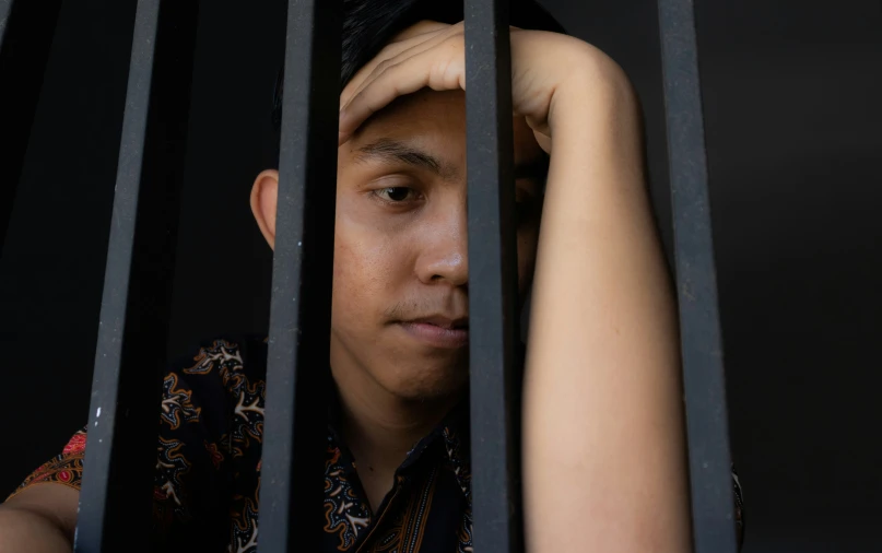 a man in patterned shirt looking through the bars of a  cell