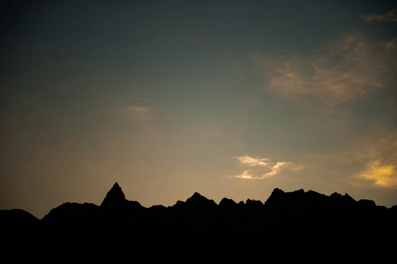 the silhouette of a mountain against a cloudy sky