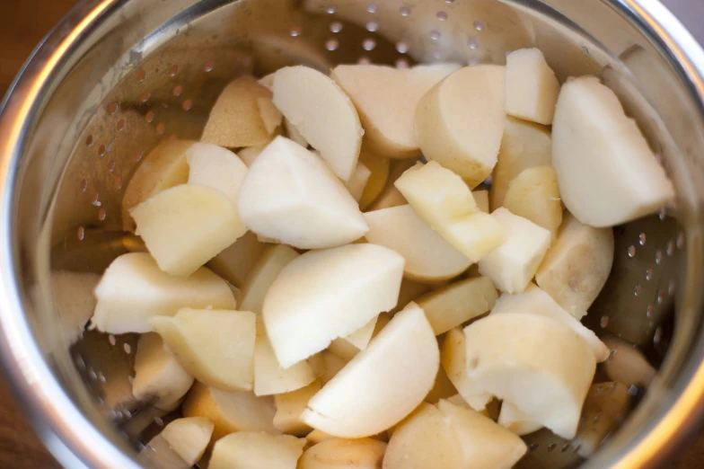 a colander full of potatoes and broth on a wooden table