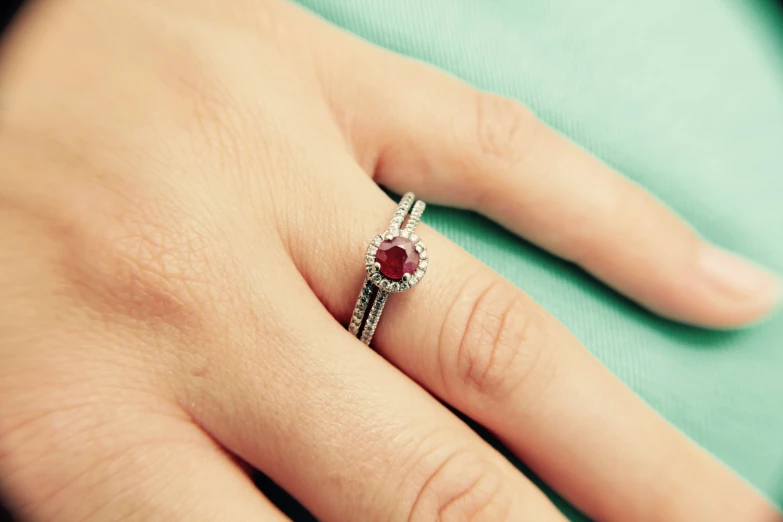 someones hand with an engagement ring with red stones on it