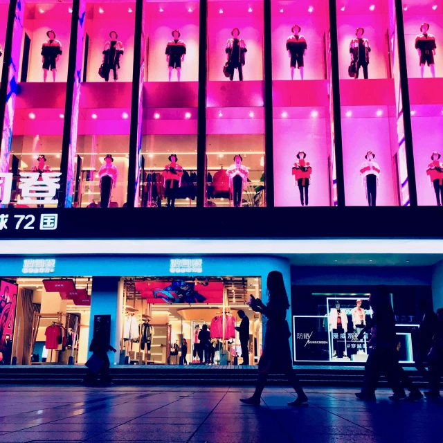 shoppers walk past the illuminated storefront of a department store