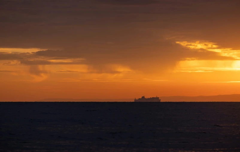 a ship sitting on the horizon during sunset