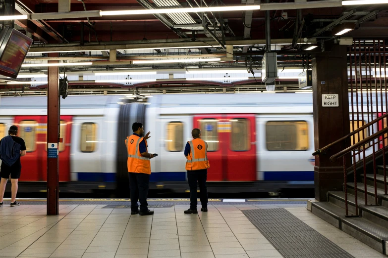 three people in vests stand on platform next to a train