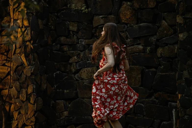 a woman in a red dress stands in front of a rock wall