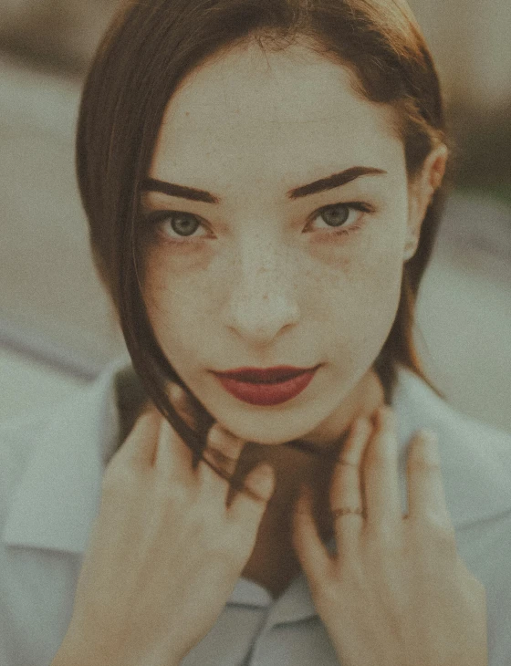 a young woman is wearing a white shirt and holding her hand near her face