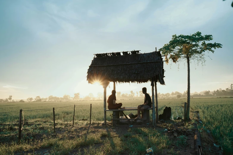 two people sitting in a small hut in a green field