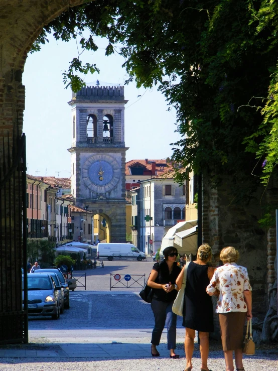 women with bags are standing at a street in front of a building and clock tower