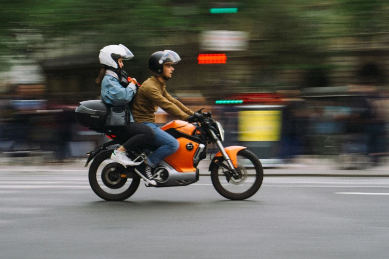 two people on an orange motor bike driving down a street