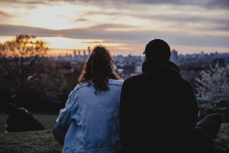 two people are sitting on a hill watching a sunset