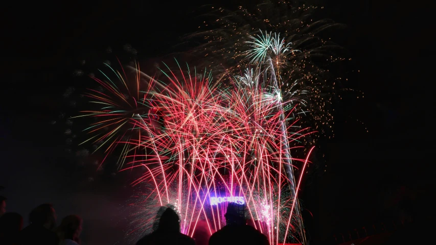 a fireworks display in the night sky with people standing near it