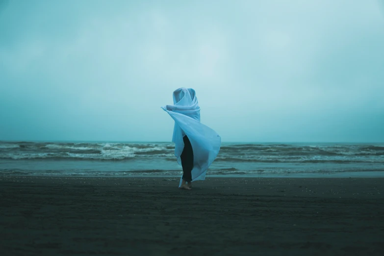 a woman holding up her veil walking along the beach