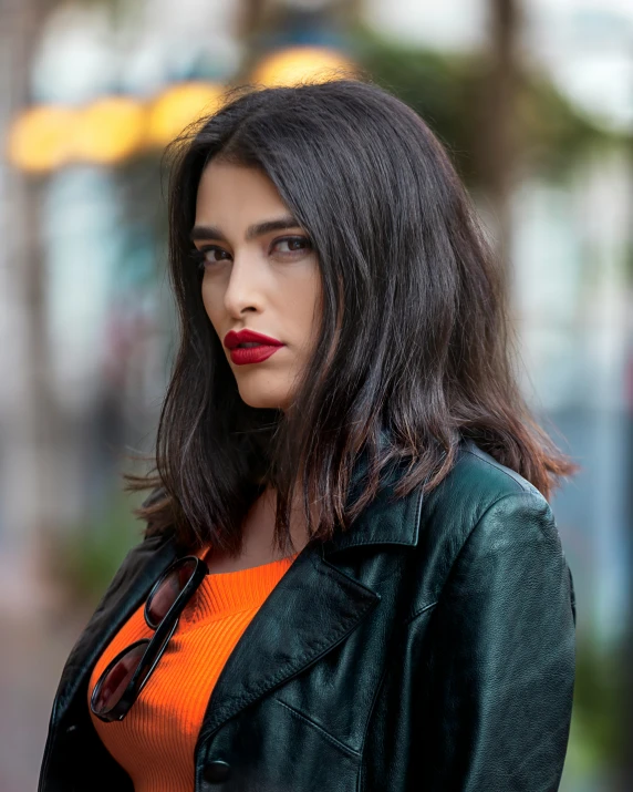 a woman wearing orange is standing outside wearing a black leather jacket