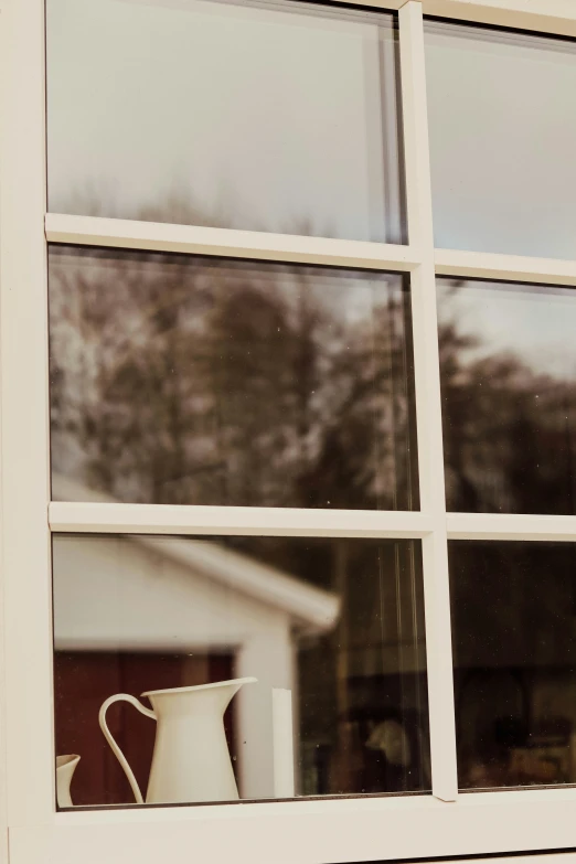 a pitcher sits by a window with a cup sitting on the ledge