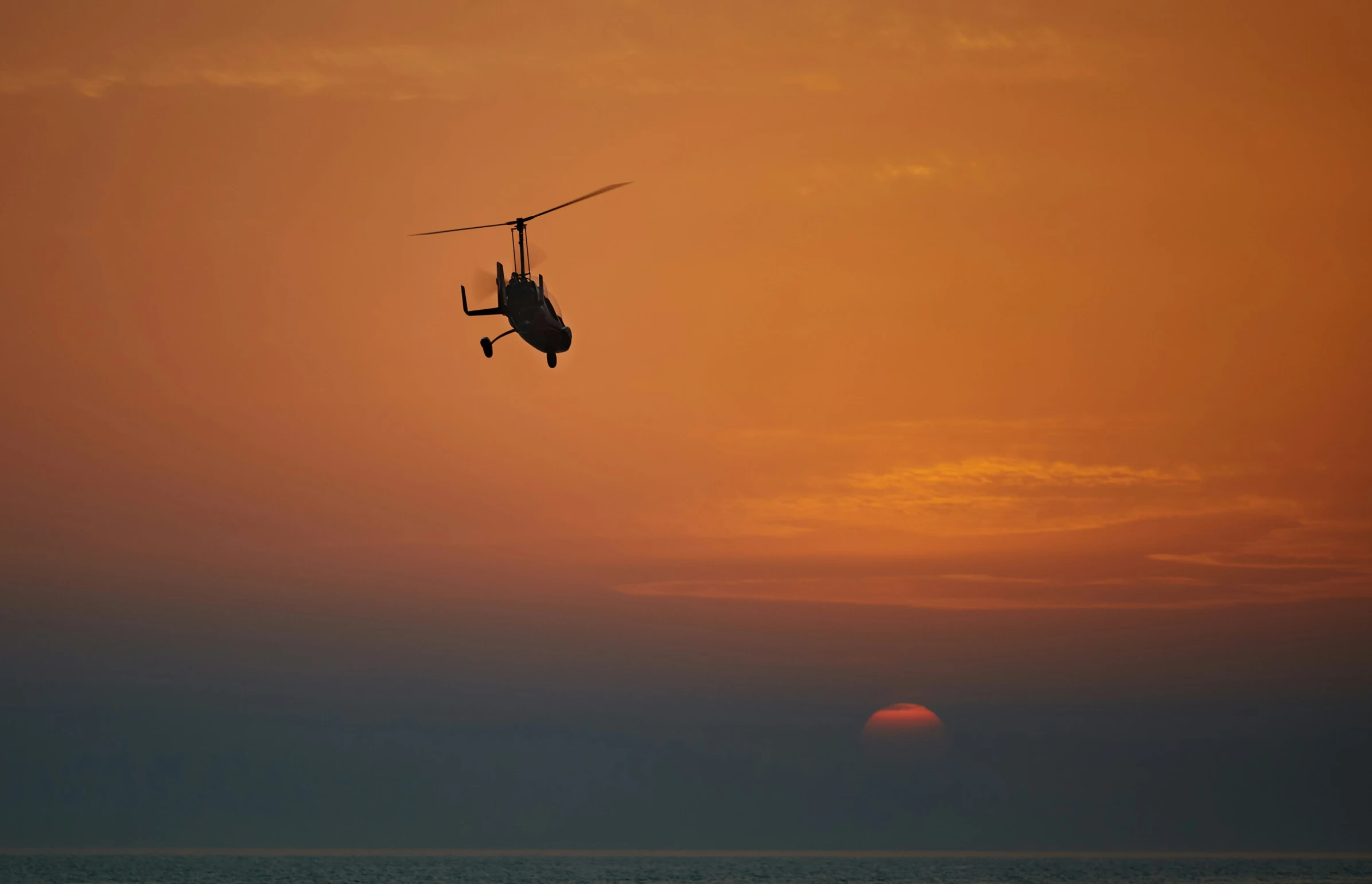 a helicopter flying with the sun setting in the background