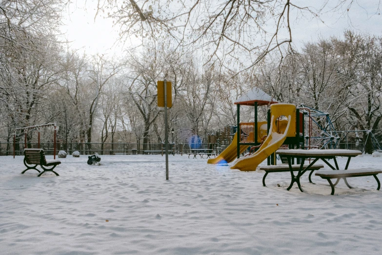 a playground with a slide, bench and snow covered ground