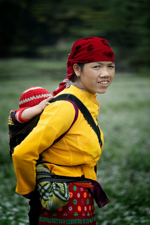 an asian lady in yellow with red shawl carrying her child