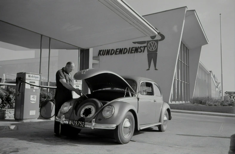 a black and white picture of a man standing next to a car with its hood open