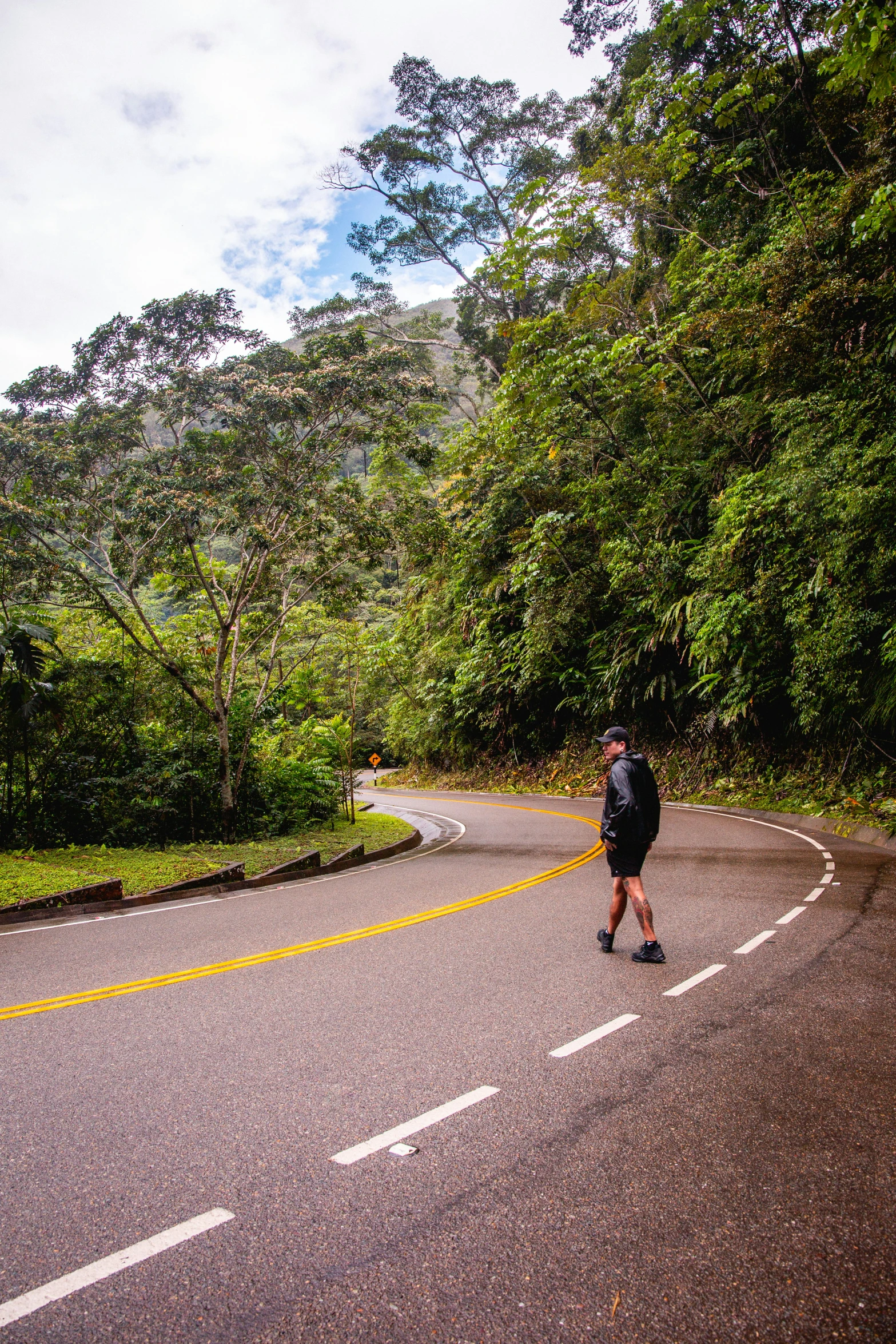 a person standing on the side of a road near a tree covered hill