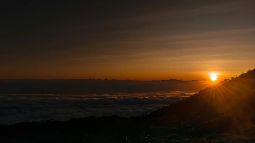 the sun rises behind some clouds and over a mountain