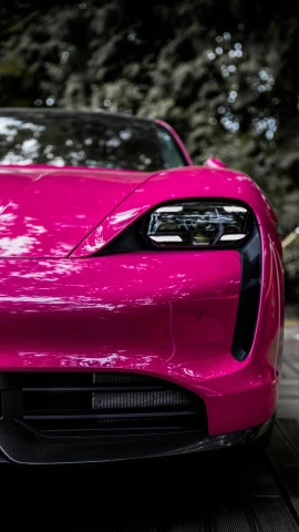 a very pretty pink colored sports car parked next to trees