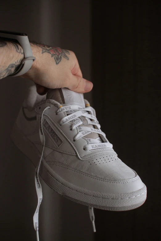 a man with tattoos holds a white sneaker