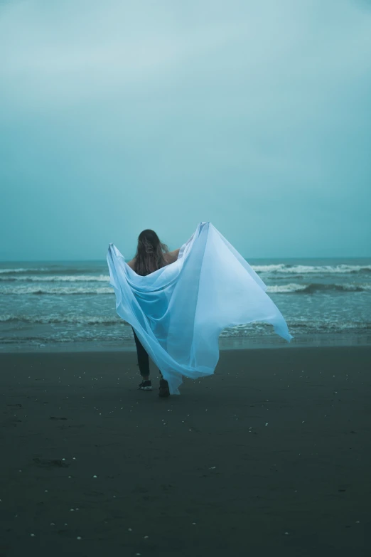 a woman on the beach holding a blue cloth in her hand