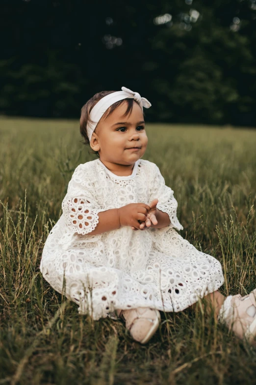 an adorable little girl sitting in a field looking into the camera