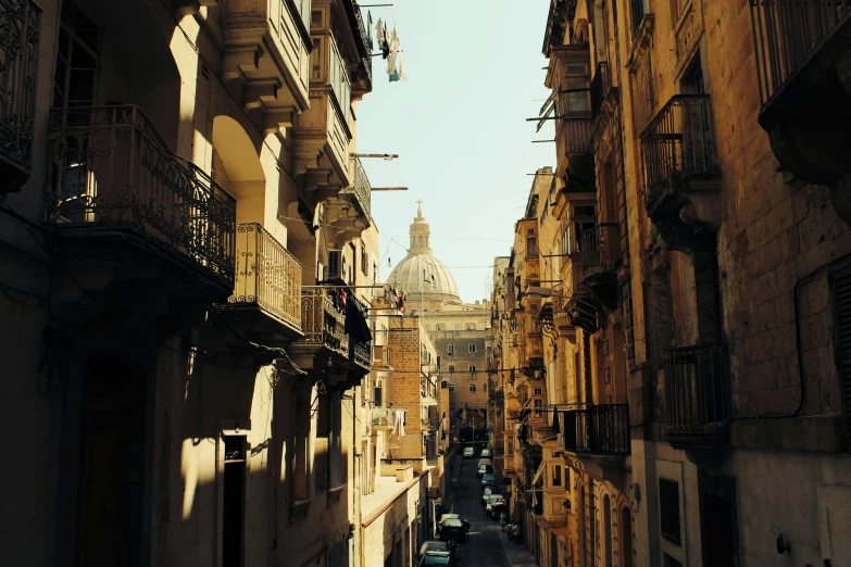 a narrow city street with various buildings, and clock tower on one side