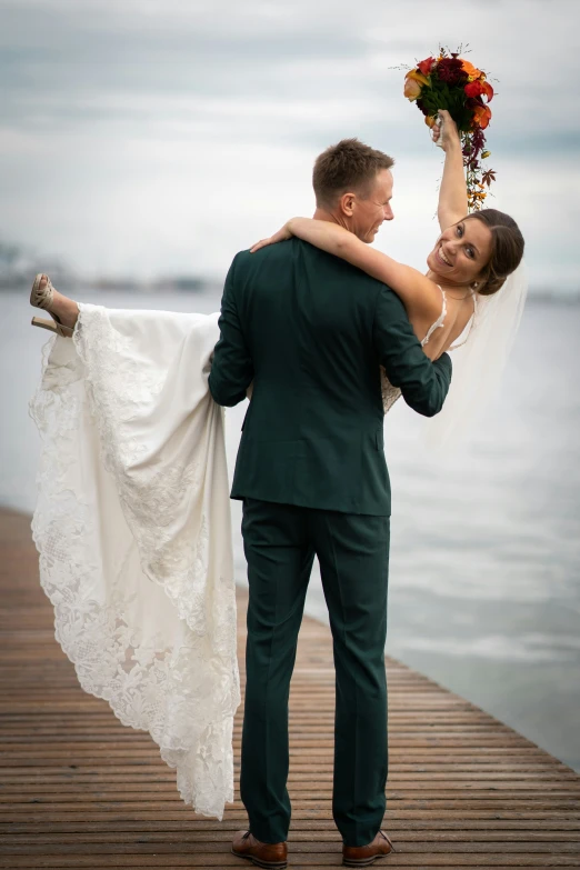 a bride carrying her groom on their shoulders, by the water