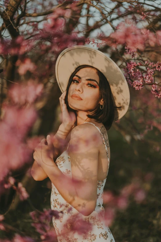 the woman is posing under some trees with her hat on