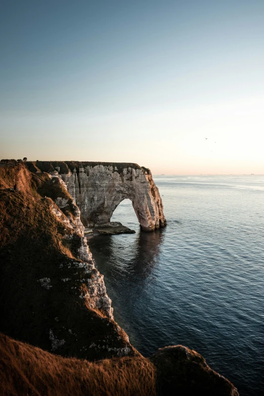 the cliffs of a cliff with a small white rock sticking out of the water